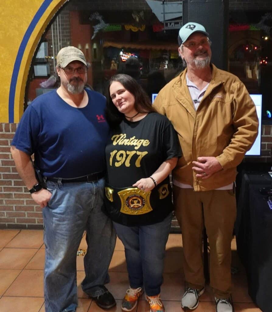 Three trivia winners holding the championship belt