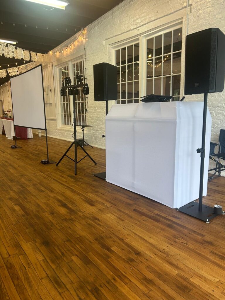 DJ booth, speakers, lights and projector screen set up at a wedding venue
